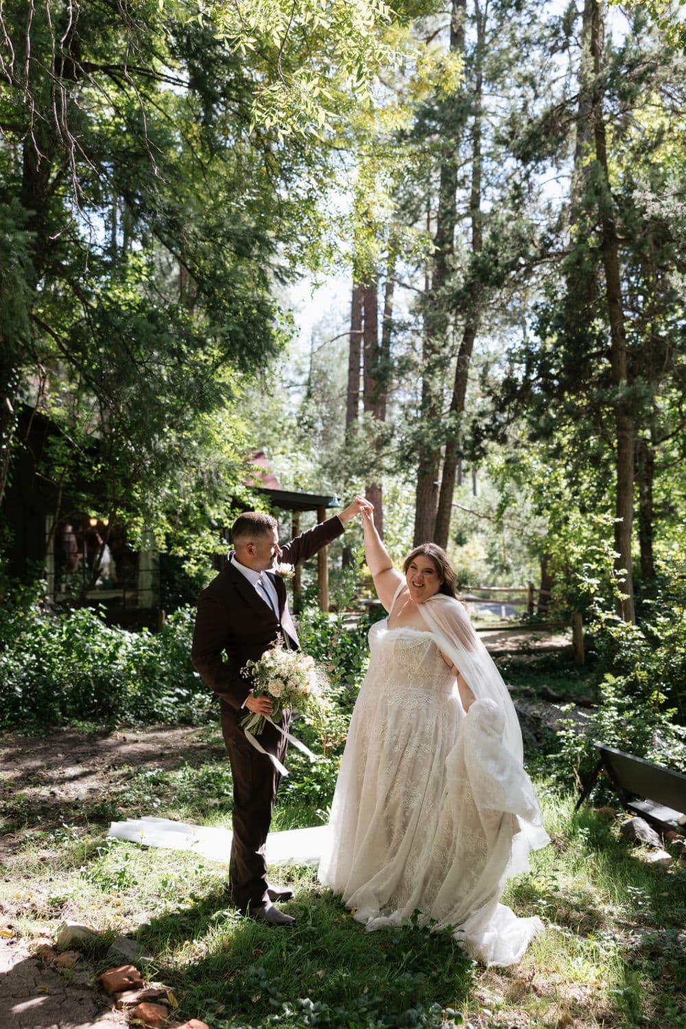 The groom twirling the bride beneath tall pines beside the cabins at Hoel Reserve